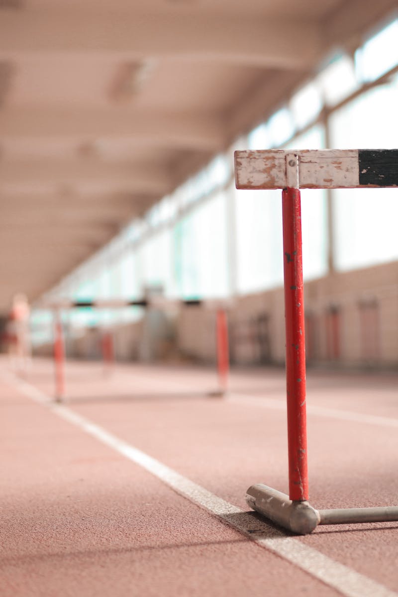 Hurdle painted in white black and red colors placed on empty rubber running track in soft focus
